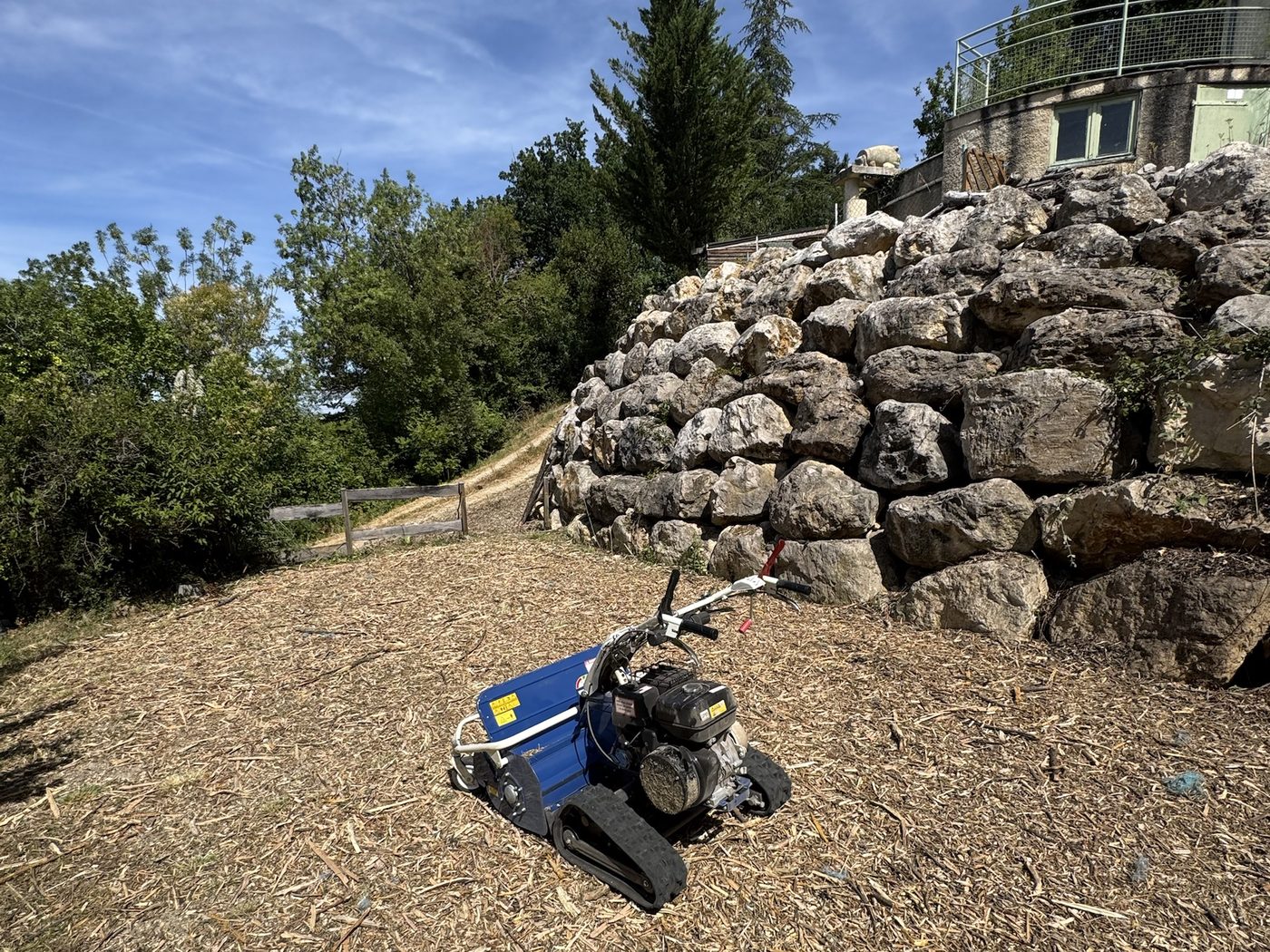 Broyeur à chenilles sur un talus débroussaillé, au pied d'un mur de gros blocs de pierre
